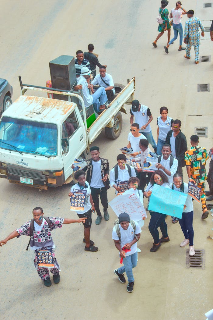A dynamic group of young people parading down the street with banners and a truck, expressing unity and excitement.