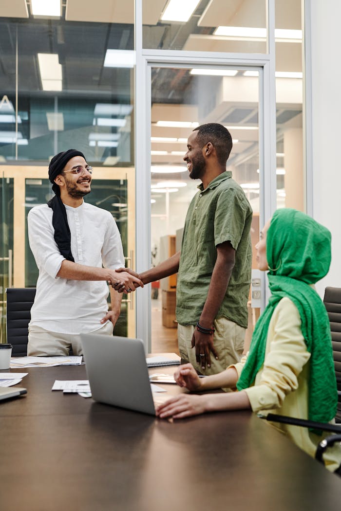 Three professionals engage in a meeting, showcasing diversity and teamwork through a handshake.
